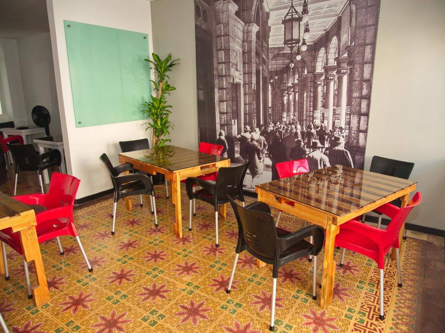 La Aldea 124: common room with wooden tables, red chairs and a mural of old photos